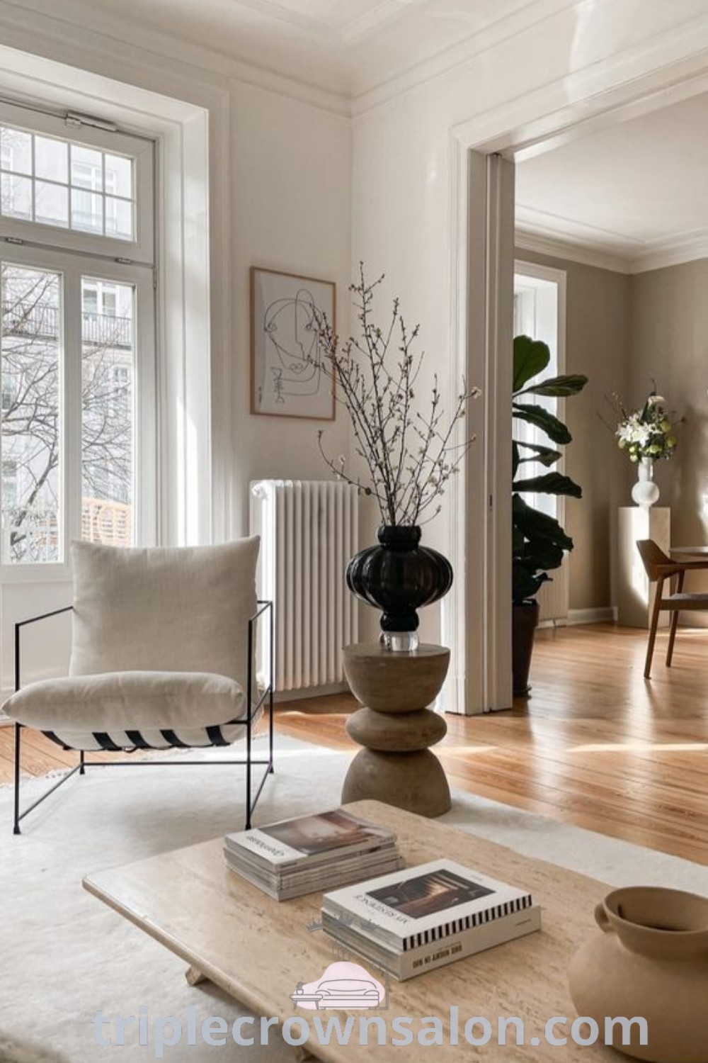 A vibrant boho-inspired living room filled with cozy decor, featuring a large window, a wooden table covered in books, and various styling elements from Japandi and vintage aesthetics. This scene offers unique design ideas for your home, showcasing inspiring decor ideas for small spaces. Discover more at triplecrownsalon.com.