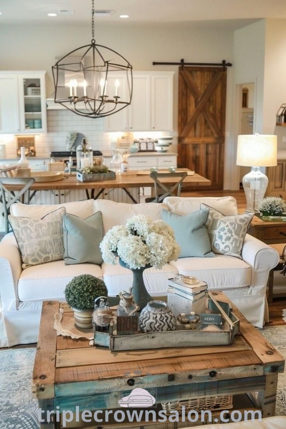 A cozy living room filled with furniture and flowers on a coffee table, representing indoor farmhouse decor with rustic Western and modern country elements. This design offers inspiring ideas for your home and unique decor inspirations, perfect for creating a warm atmosphere. Visit triplecrownsalon.com for more decor tips.